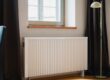 Hvit veggmontert radiator under et vindu i en bolig
