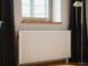 Hvit veggmontert radiator under et vindu i en bolig
