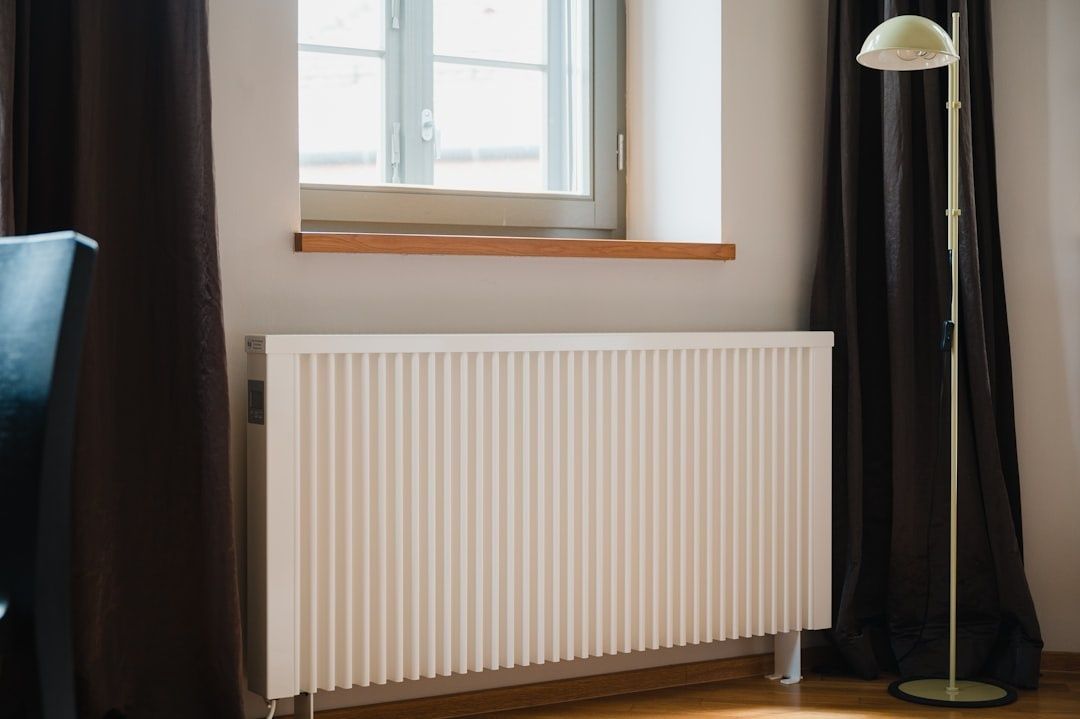 Hvit veggmontert radiator under et vindu i en bolig
