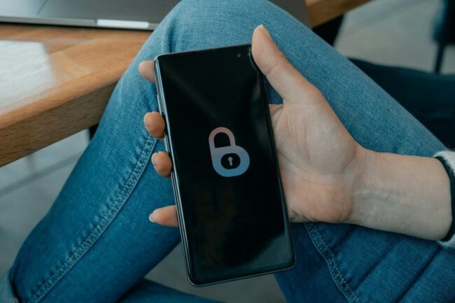 Hånd holder en smarttelefon med et låst hengelåsikon på skjermen